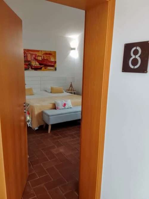 Entrada do Quarto 8 na Pousada Cerro da Campaniça em Santiago do Cacém, com moldura de porta laranja, paredes brancas e cama amarela