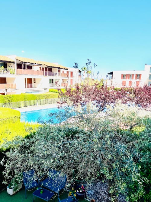 Vue piscine de l'appartement Home Guardian Services à Sant Jordi avec jardins, bâtiments blancs et corail, ciel bleu
