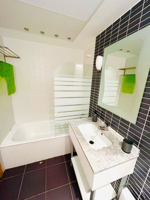 Salle de bain moderne avec mur d'accent en carrelage noir, meuble vasque blanc et douche vitrée dans l'appartement Sant Jordi