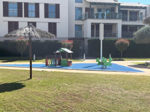 Complexe Sant Jordi avec aire de jeux bleue, parasol couvert, pelouse verte surplombant la zone piscine