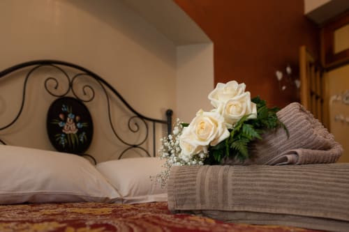 Cream roses and baby's breath arranged on grey linens beside ornate iron headboard in Casa Scola Loano's Manin room