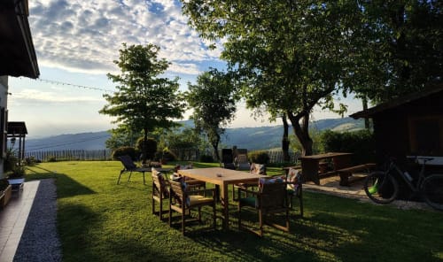 Suggestivo patio all'aperto del B&B Monte Adone a Monzuno con tavolo da pranzo in legno, prato verde e vista sulle montagne.