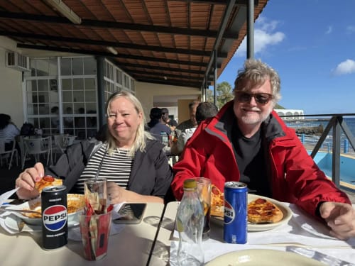 Dois hóspedes jantando ao ar livre na Golden Mermaid Villa em Ribeirinha, com vista para o mar, saboreando pizza e Pepsi