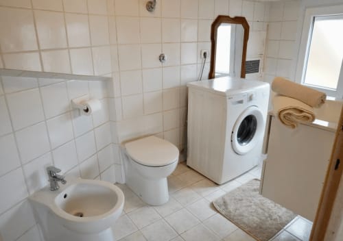 Bagno pulito presso Di Leonardo Bnb a Velletri con piastrelle bianche, lavandino, toilette, lavatrice e specchio