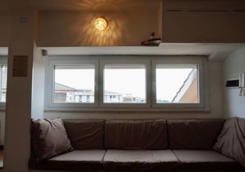 Elegante soggiorno moderno con divano marrone, tre ampie finestre con vista sulla città, lampadario decorativo, Di Leonardo BnB