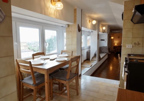 Zona pranzo dell'appartamento Di Leonardo Bnb a Velletri con tavolo in legno, vista sulla città dalle finestre e cucina moderna visibile