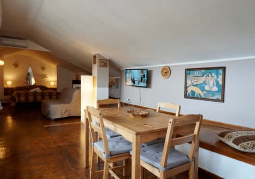 Spaziosa mansarda a Velletri con tavolo in legno, zona giorno e camera da letto, illuminazione calda e vista sulla città.