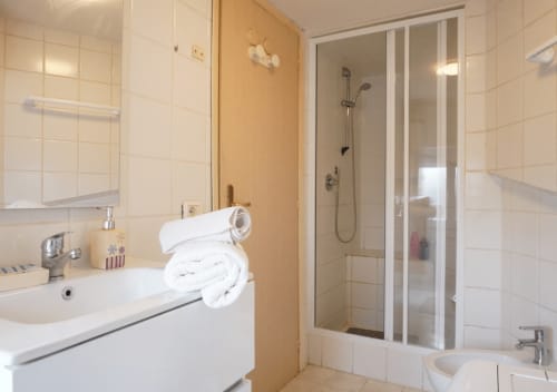 Bagno pulito con piastrelle bianche, lavabo con specchio, cabina doccia e asciugamani bianchi al Di Leonardo B&B a Velletri