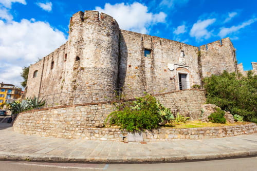 Antica fortezza in pietra con torre a La Spezia, circondata da vegetazione e cielo azzurro