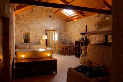 Rustic stone interior of Casa Rural A Bouciña in Hío, Spain, featuring wooden beams, fireplace, and warm lighting