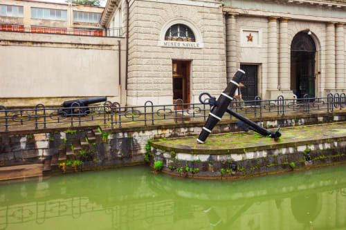 Museo navale di La Spezia con scultura d'ancora sopra l'acqua del canale verde e l'architettura storica in pietra