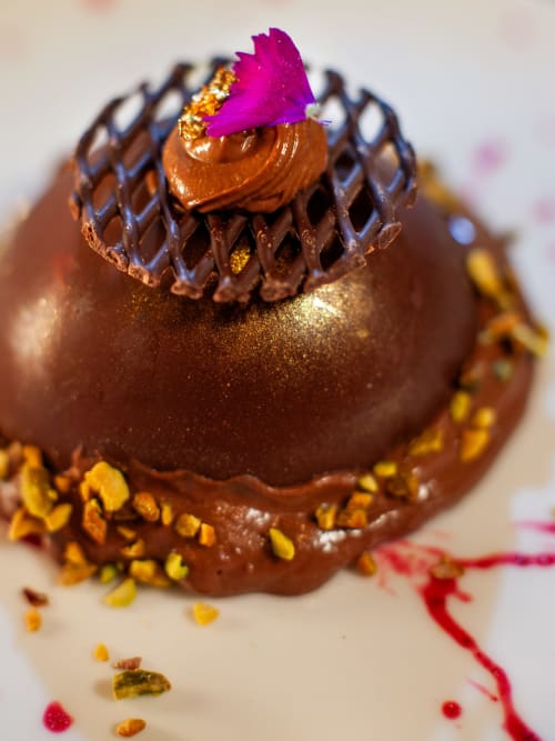 Elegante postre de chocolate con flor magenta y detalles dorados en Casa Grande do Soxal