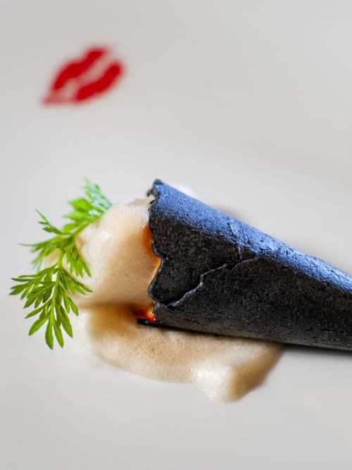 Plato gourmet de Casa Grande do Soxal con entrada cubierta de carbón, hierbas frescas y salsa roja