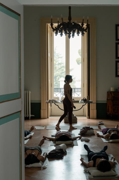 Lezione di yoga a Villa Ceci ad Andria con partecipanti su tappetini e istruttore in piedi, lampadario nero sopra