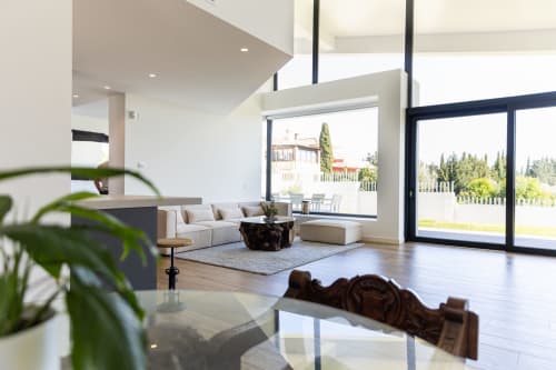 Salón de lujo moderno en hotel BH Marbella con ventanales panorámicos, mobiliario contemporáneo y vistas al jardín mediterráneo