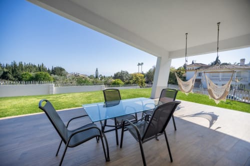 Patio cubierto de BH Marbella con mesa de cristal, sillas negras y vistas al campo de golf