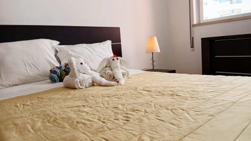 Quarto Sweet Home em Portimão com almofadas brancas, pelúcias, roupas de cama bege e luminária de cabeceira