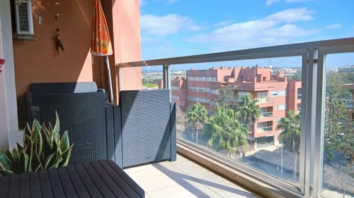 Varanda ensolarada no Sweet Home Portimão com vista para o rio, com assentos e plantas em vasos frente aos edifícios de tijolos