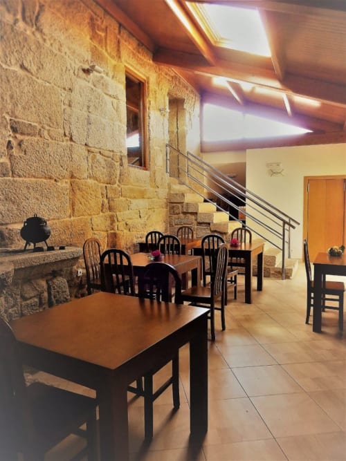 Rustic dining area at Casa Rural A Bouciña with stone walls, wooden tables, and metal stair railings in Hío