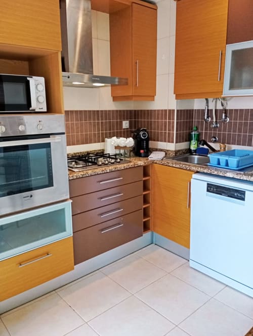 Cozinha moderna do apartamento Sweet Home Borralha em Portimão com armários laranja, bancadas de granito e eletrodomésticos em aço inoxidável