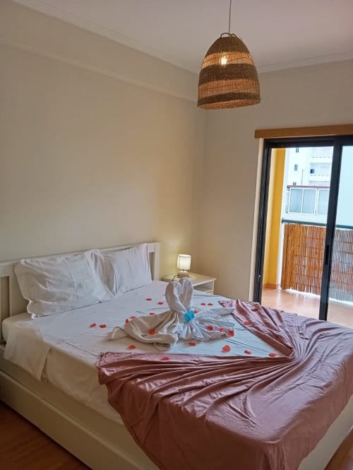 Quarto romântico na Sweet Home Borralha, Portimão com cama decorada, luminária pendente trançada e vista para a cidade do balcão