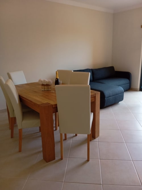 Sala de estar moderna com mesa de jantar em madeira, cadeiras bege e sofá seccional azul em Portimão