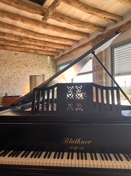 Grand piano noir dans une villa aux poutres en bois apparent et murs en pierre à Gîte l'Harmonie du Causse