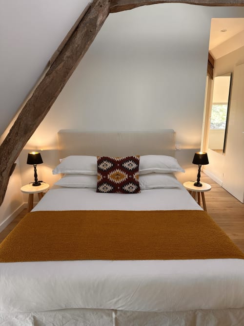 Chambre mansardée au Gîte l'Harmonie du Causse avec poutre bois rustique, literie blanche, coussin à motifs et éclairage chaleureux