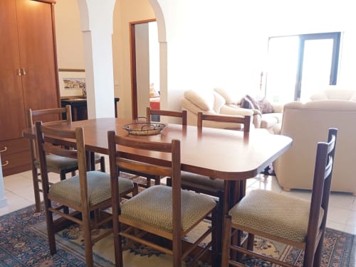 Sala de jantar com mesa e cadeiras de madeira, sala de estar com sofá creme, portas em arco no apartamento Sweet Home Vila Rosa