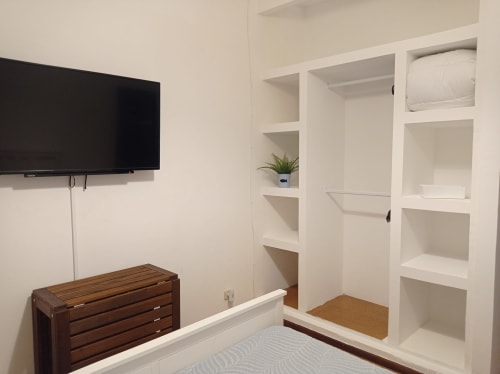 Quarto moderno no Sweet Home Inn Portimão com TV de parede, prateleiras embutidas, cômoda de madeira e closet.