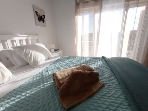 Quarto ensolarado em Sweet Home Portimão com roupa de cama branca, manta turquesa, toalha marrom e vista para a cidade
