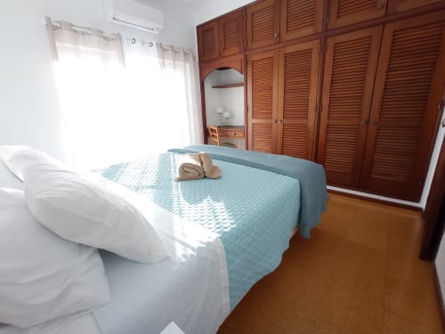 Quarto bem iluminado no Sweet Home em Portimão com camas individuais, roupa de cama azul, guarda-roupa de madeira e vista para a cidade