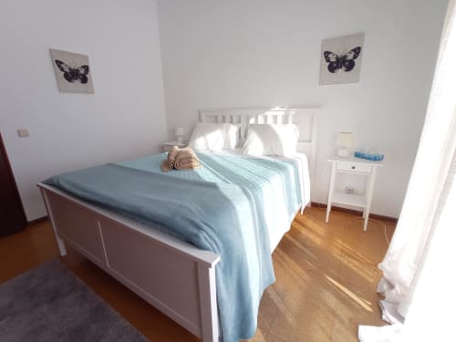 Quarto luminoso no hotel Sweet Home em Portimão com cama branca, roupas de cama azuis, arte com borboletas e pisos de madeira
