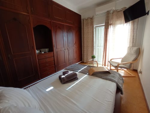 Bright bedroom at Sweet Home in Portimão with double bed, wooden wardrobe, armchair, and city views