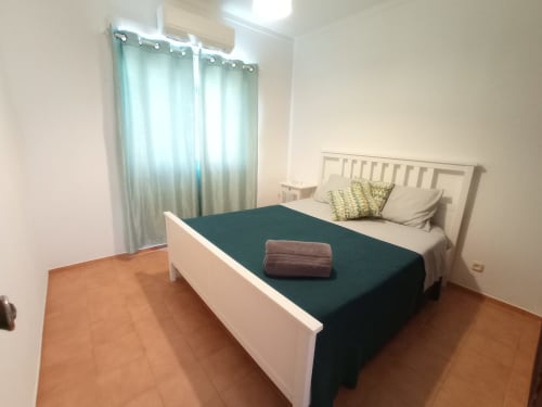 Quarto moderno no Sweet Home Inn Terrace em Portimão com cama branca, cobertor verde escuro e vista para a cidade