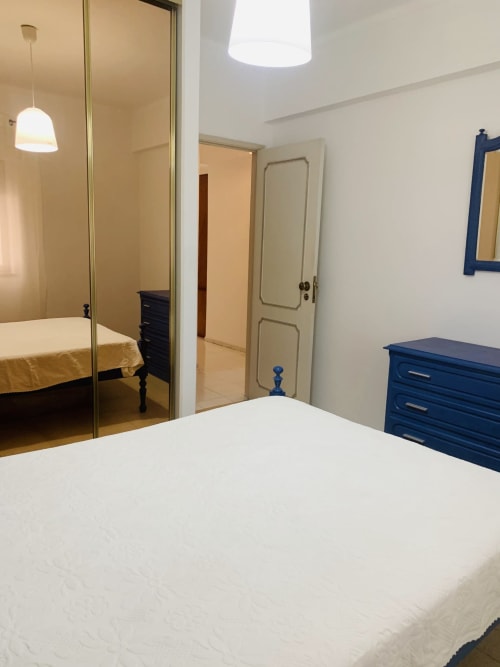 Quarto moderno com cama branca, cômoda azul e guarda-roupa espelhado no hotel Sweet Home em Portimão