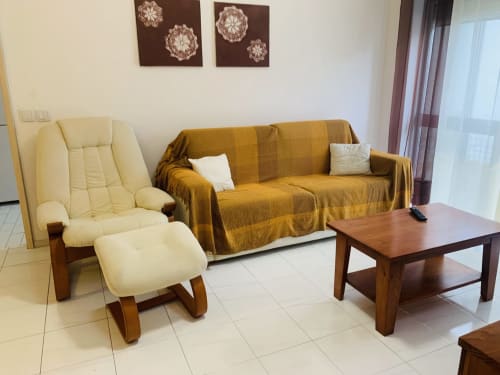 Sala de estar moderna do hotel Sweet Home em Portimão com poltrona creme, sofá mostarda, mesa de centro de madeira e elementos decorativos