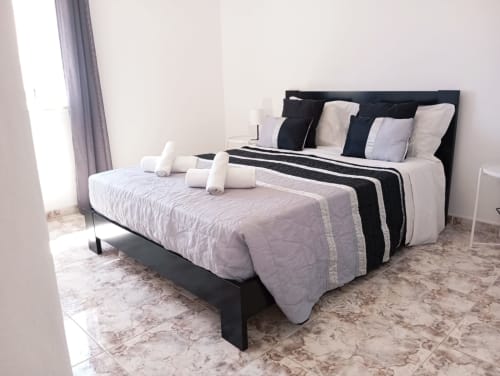 Quarto moderno no Sweet Home Portimão com cama de estrutura preta, roupa de cama branca e preta, piso de mármore e vista para a cidade.