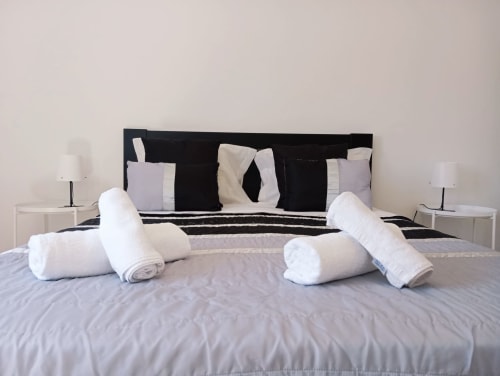 Quarto moderno em Sweet Home Portimão com cabeceira preta, toalhas brancas enroladas e vista para a cidade
