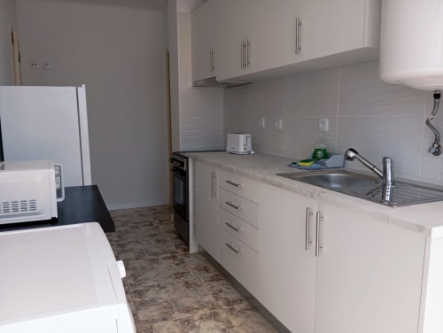 Cozinha moderna em Sweet Home Portimão com armários brancos, pia em aço inoxidável e painel de azulejos