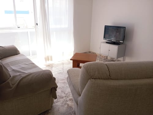 Quarto estúdio luminoso na Sweet Home Portimão com sofá bege, cama, TV, mesa de madeira e vistas da cidade
