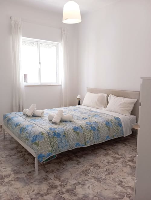 Quarto iluminado no Sweet Home hotel em Portimão com cama de flores azuis, almofadas brancas e vista para a cidade