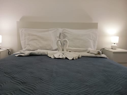 Quarto do Sweet Home Portimão com cisne em toalha, travesseiros brancos, roupa de cama texturizada escura e luminária de cabeceira