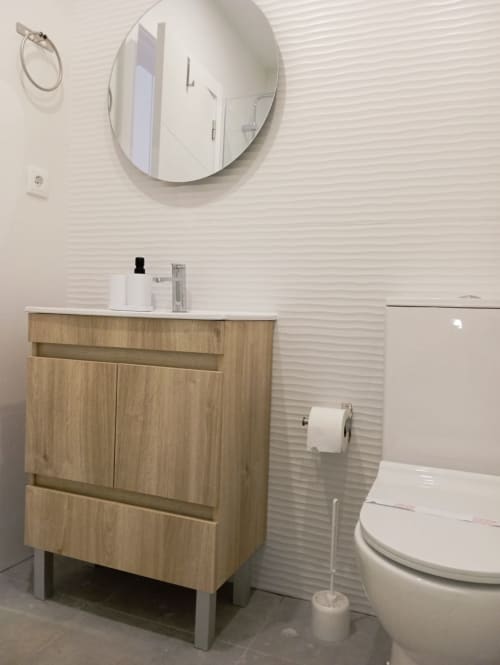 Banheiro moderno do apartamento Sweet Home em Portimão com gabinete de madeira, espelho redondo, vaso sanitário branco e azulejos texturizados