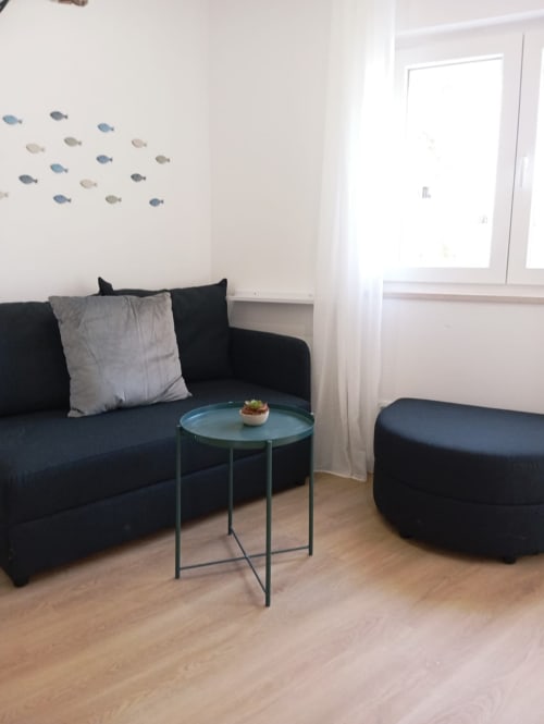 Sala de estar moderna no apartamento Sweet Home Portimão com sofá preto, mesa lateral azul-petróleo e arte decorativa de peixe na parede