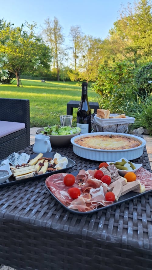 Outdoor garden dinner spread at Traînefeuilles B&B featuring charcuterie, quiche, wine and fresh salad with green lawn views