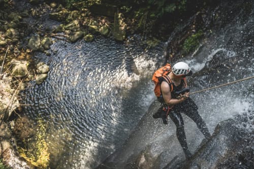 Adventurer canyoning in Madeira waterfall with rope and safety gear near Ribeira Brava