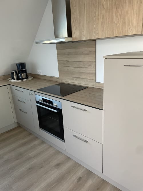 Cuisine moderne avec armoires blanches, plan de travail en bois, plaque à induction et four en acier inoxydable à La clé des vignes