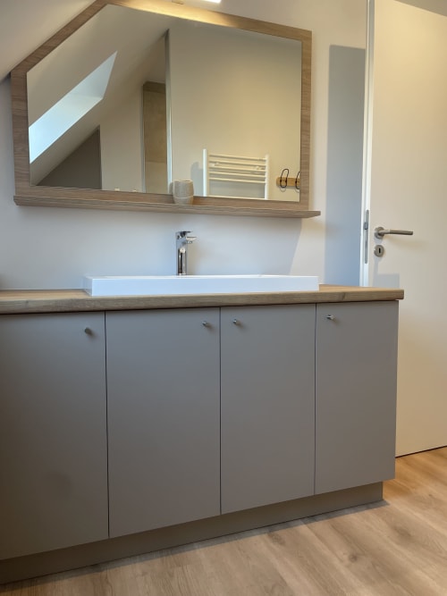 Salle de bain moderne avec meubles gris, lavabo blanc, plan de travail en bois et miroir encadré à La clé des vignes
