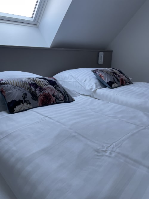 Chambre moderne avec literie blanche et oreillers floraux décoratifs dans l'appartement de Ribeauvillé